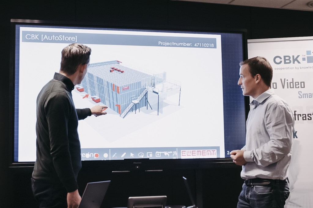To menn peker og ser på en presentasjon med en tegning av en AutoStore-løsning.