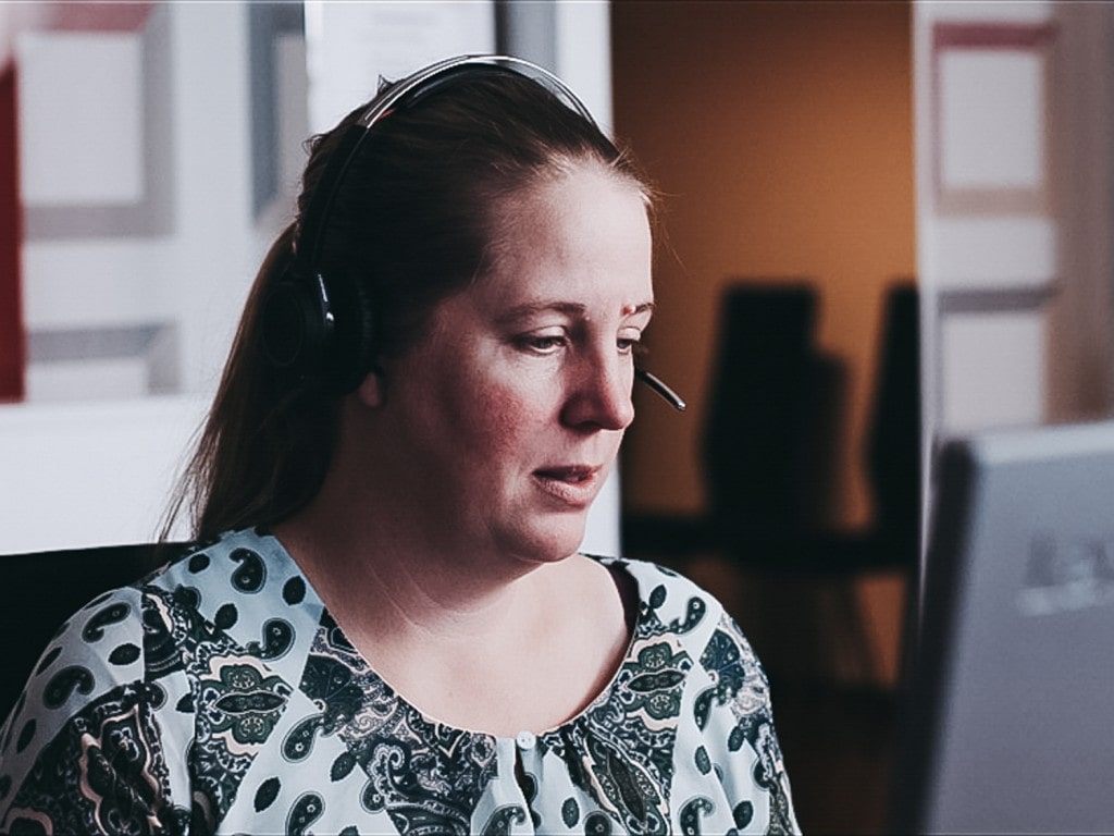 Et nærbilde av en kvinne som prater i hodetelefoner foran en dataskjerm.