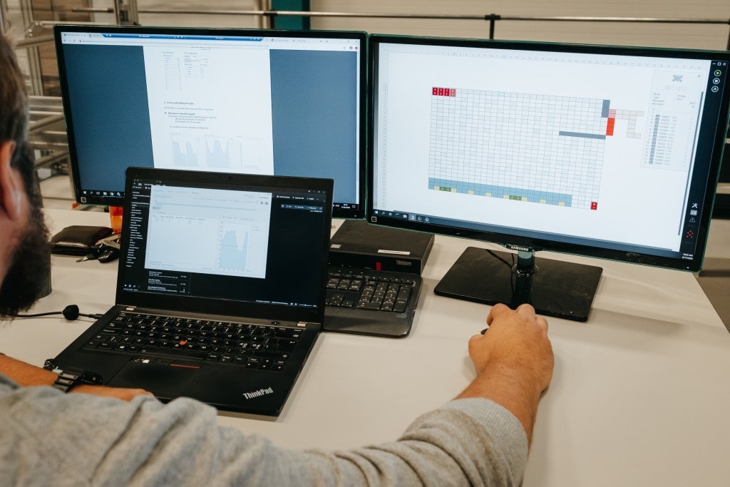 En mann jobber med en AutoStore-løsning med tre dataskjermer.