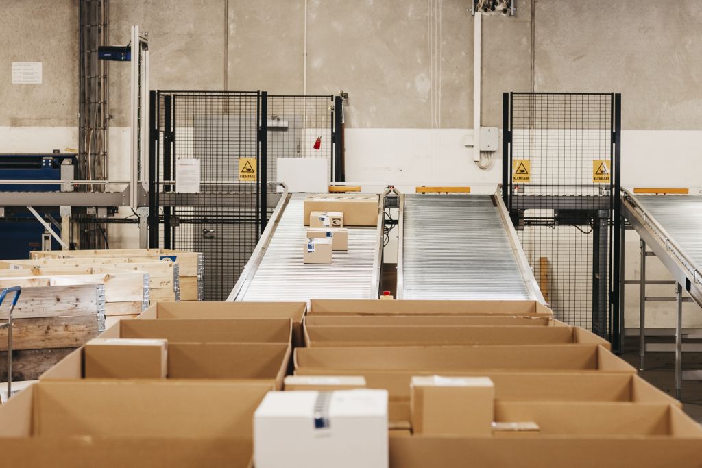 Pakker transporteres på samlebånd i et automatisert lager.